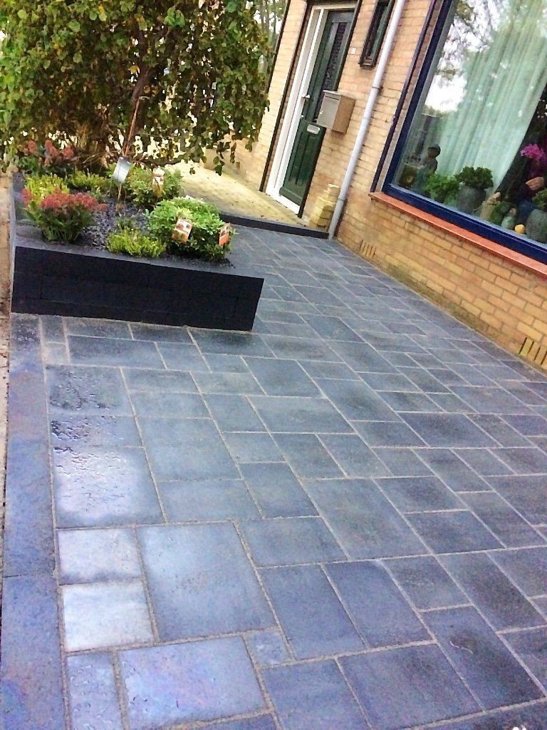 Donkergrijs betegeld terras met een zwarte plantenbak en een bakstenen gebouw op de achtergrond.