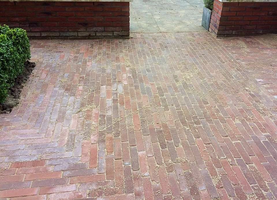 Een terras van bakstenen met een visgraatpatroon, omgeven door bakstenen muren en groen.