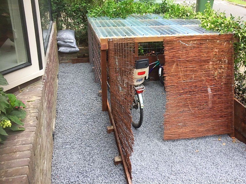 Fietsenstalling van hout en geweven materiaal, grijze grindondergrond, fiets erin.