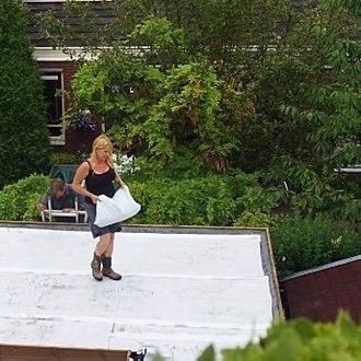 Vrouw op een plat dak met een witte tas in haar hand, bomen op de achtergrond.