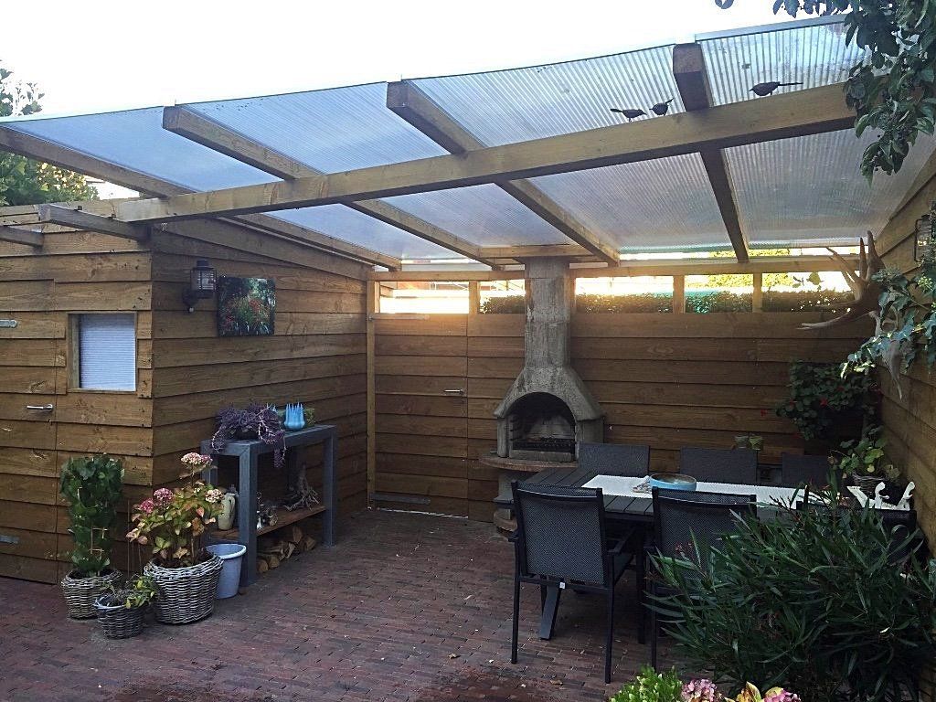Houten terras met doorschijnend dak, ingebouwde barbecue, eettafel en omringende houten schutting.