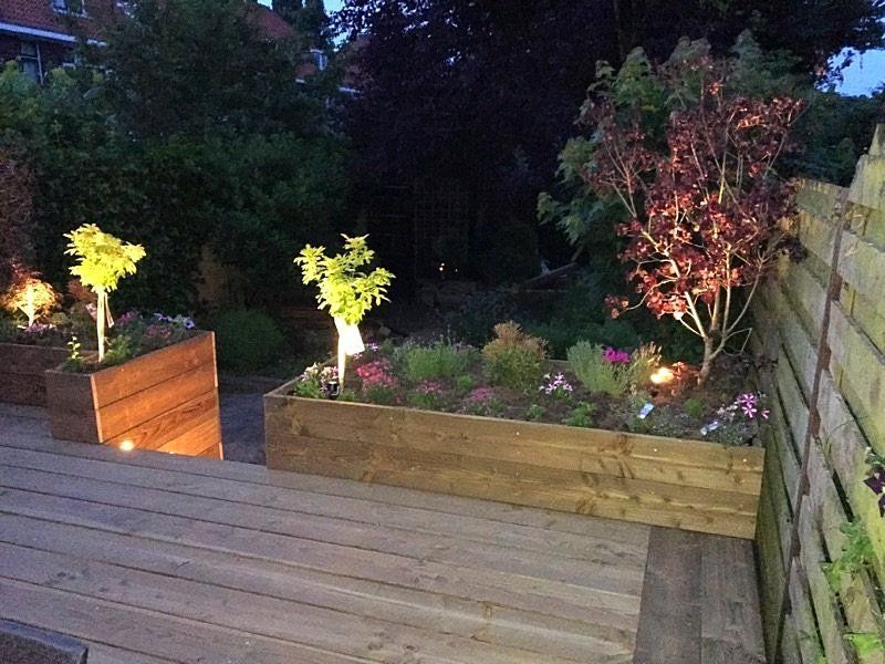 Houten plantenbakken met verlichte planten op een terras bij schemering.
