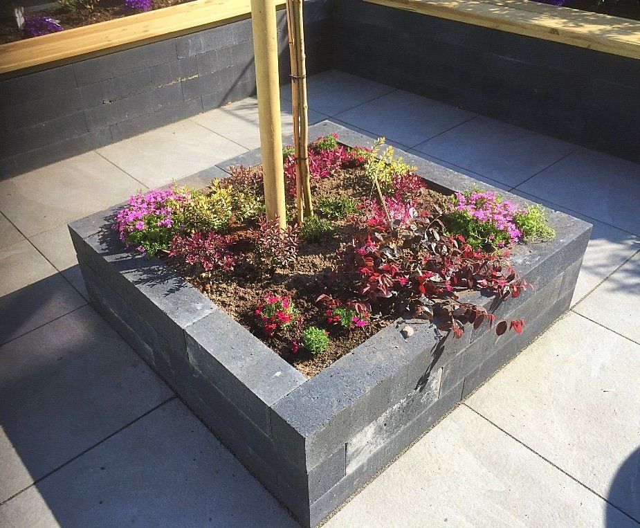 Vierkante plantenbak met bloemen en een klein boompje op een terras.