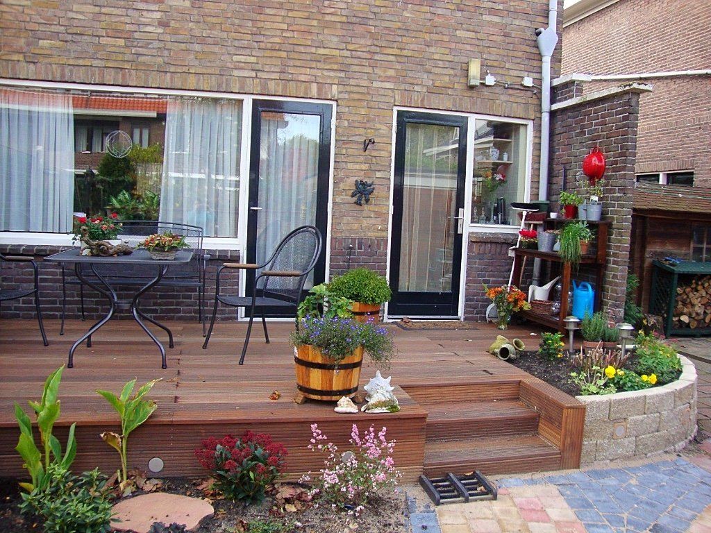 Houten terras met tuinmeubilair, planten, een bakstenen muur en openslaande deuren.