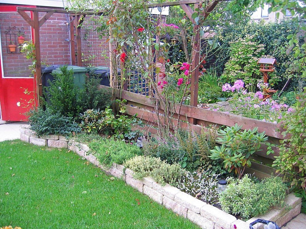 Een bloembed met een stenen rand, gevuld met planten en bloemen, naast een grasveld en een houten schutting.