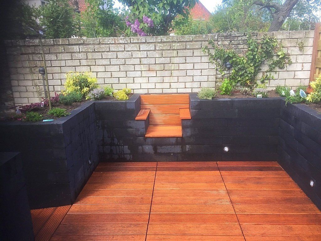 Houten terras met donkere stenen muren, een trap en een lichte bakstenen muur op de achtergrond. Groen.