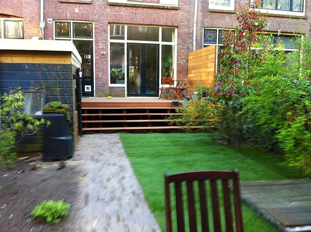 Achtertuin met houten terras en trap naar het huis, groen gazon en tuin.