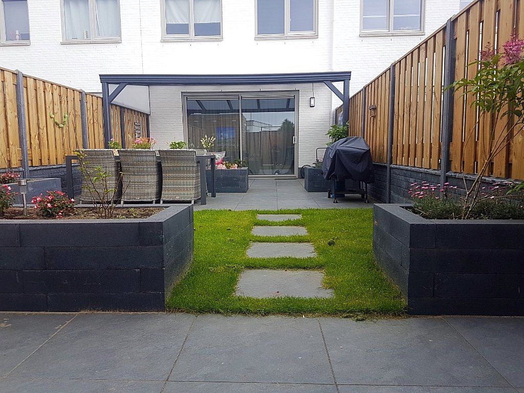 Terras in de achtertuin met een pad door het gras, plantenbakken en een overdekte zithoek.