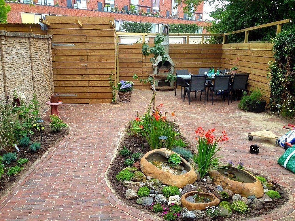 Een terras in de achtertuin met een bakstenen pad, een houten schutting, een eethoek en een kleine tuin met stenen accenten.