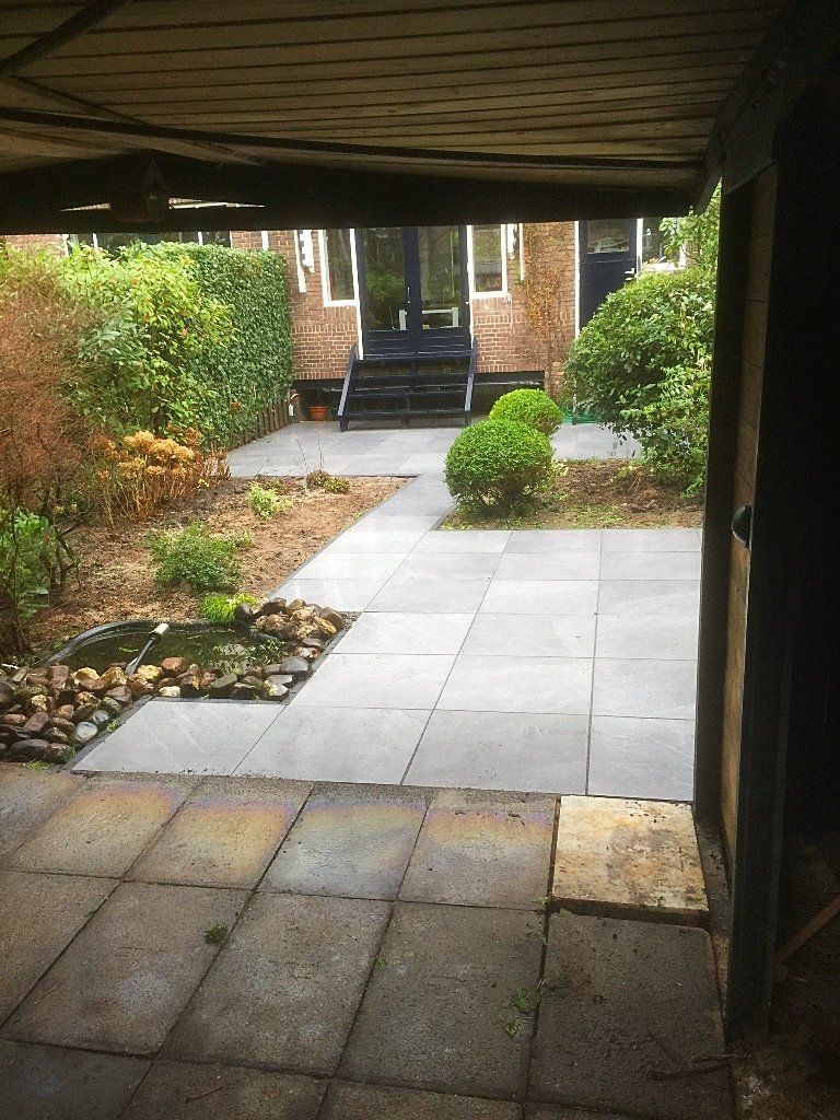 Terras met stenen bestrating dat naar een huis leidt, een tuin met een kleine vijver en weelderig groen.
