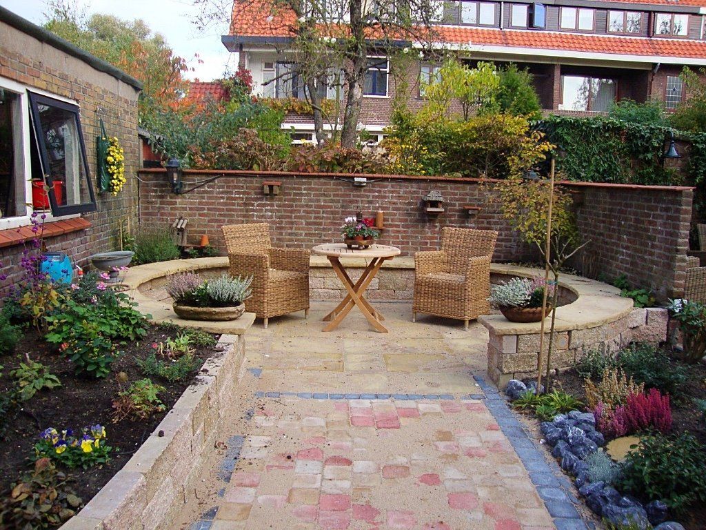 Bakstenen terras met rieten stoelen, tafel en bloembedden; bakstenen muur op de achtergrond, woonomgeving.