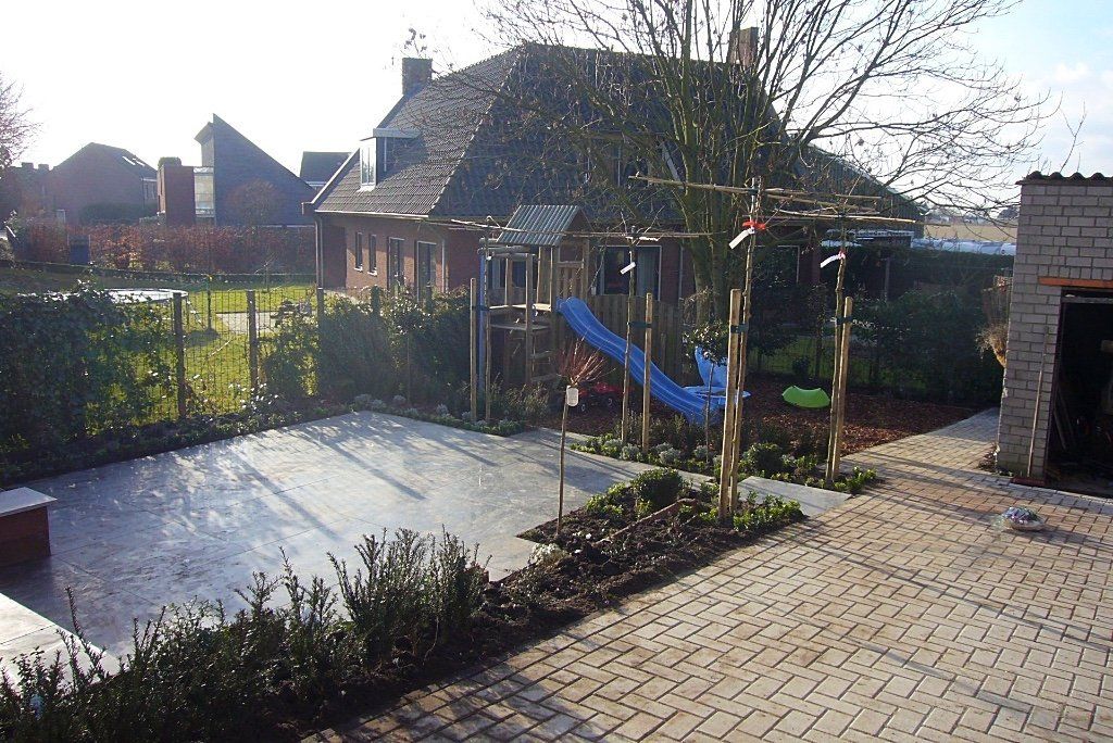Achtertuin met betegeld terras, speeltoestel met glijbaan en stenen huisje.