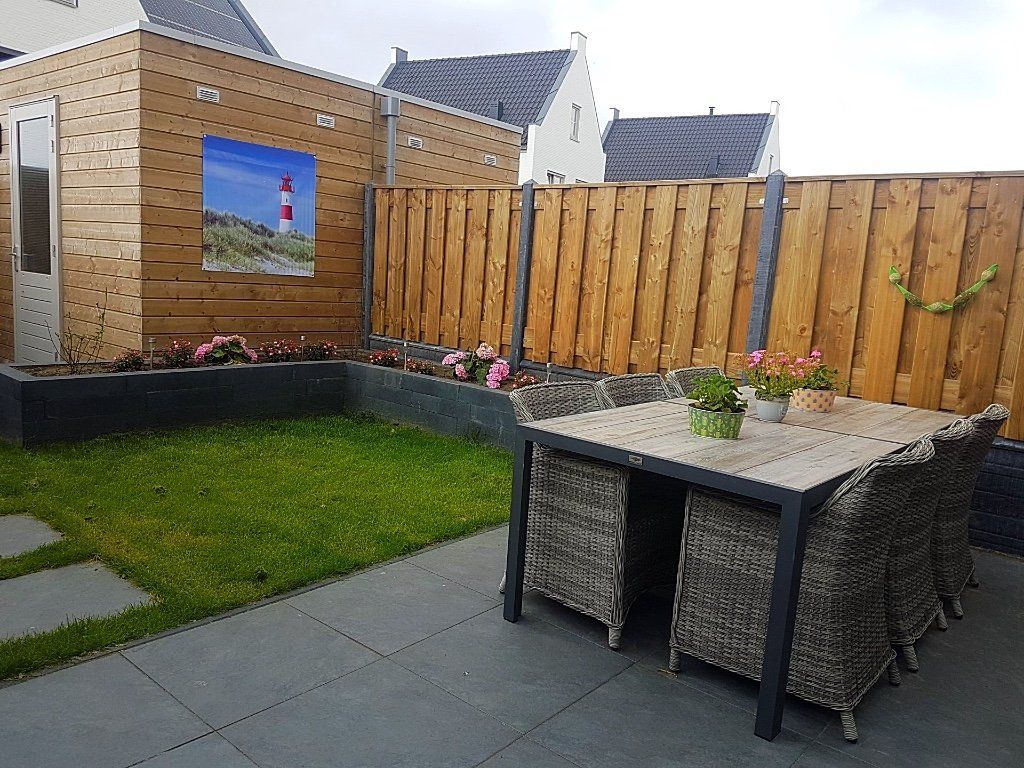 Achtertuin met terras, gazon, houten schutting, tafel met stoelen en een afbeelding van een vuurtoren.