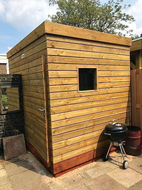 Houten schuur met horizontale planken als gevelbekleding, een klein raam en een barbecue.