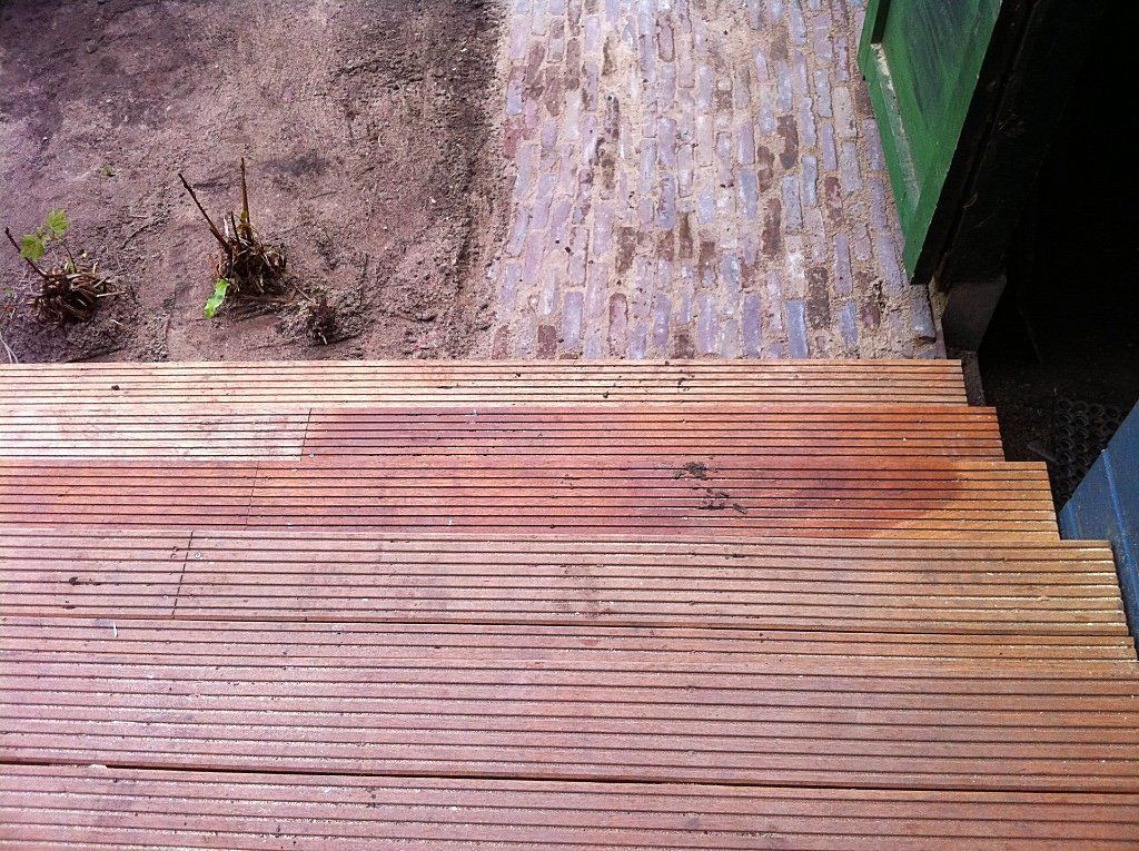 Houten trappen naar beneden, een nat bakstenen pad en een stukje grond.