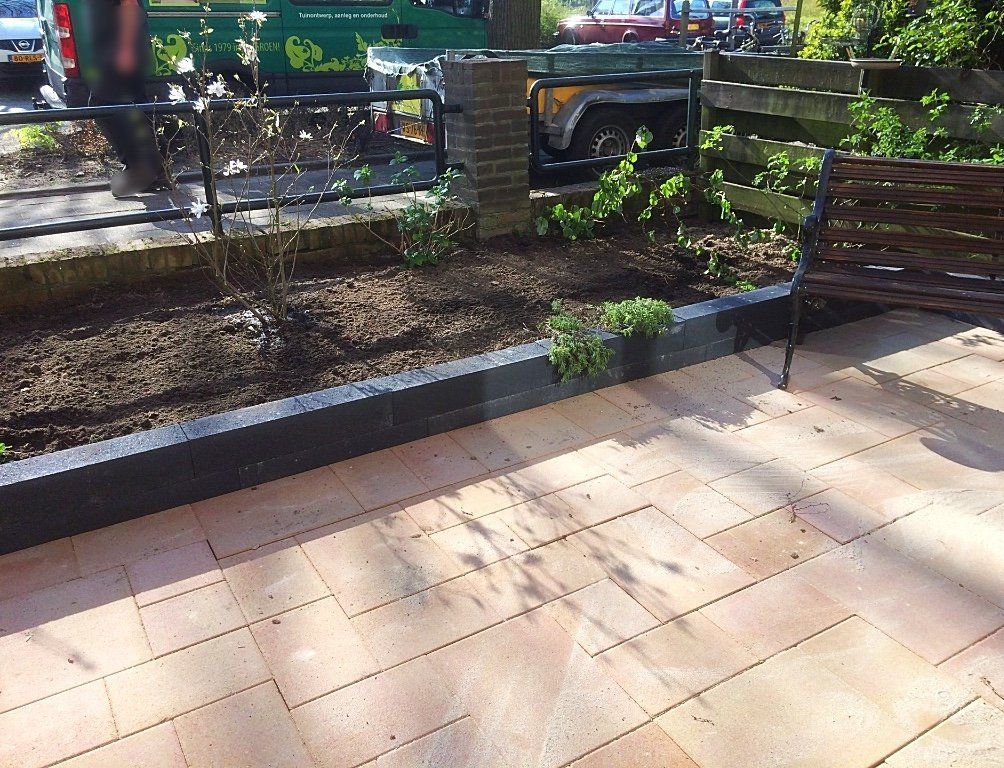 Terras met een verhoogd bloembed en een houten bank. In het bloembed staan ​​pas geplante struiken.