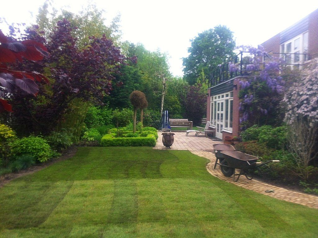 Een keurig onderhouden achtertuin met gazon, bloemperken, terras en een huis met twee verdiepingen.