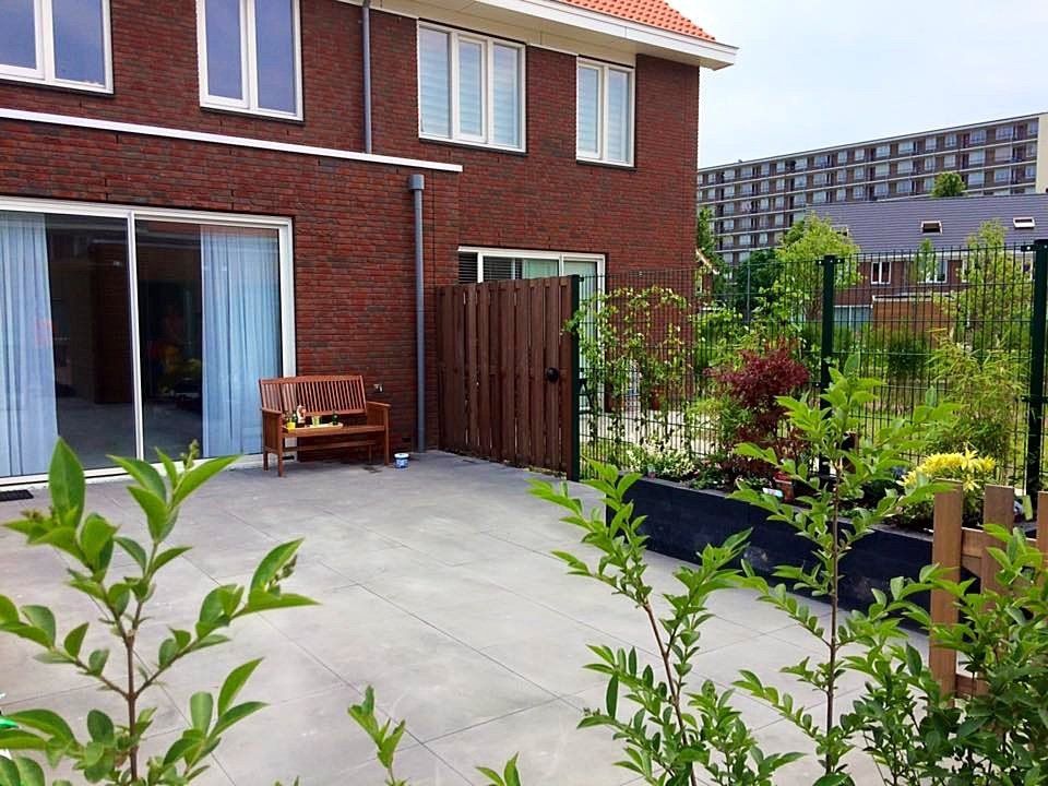 Bakstenen huis met terras en tuin, houten schutting, groenvoorziening en verhoogde bloembedden.