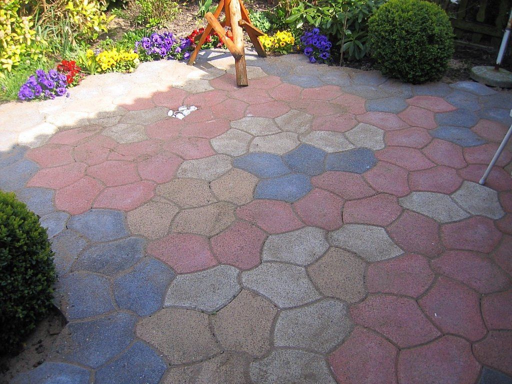 Kleurrijke, in elkaar grijpende terrastegels in een tuinomgeving, omgeven door bloemen en struiken.