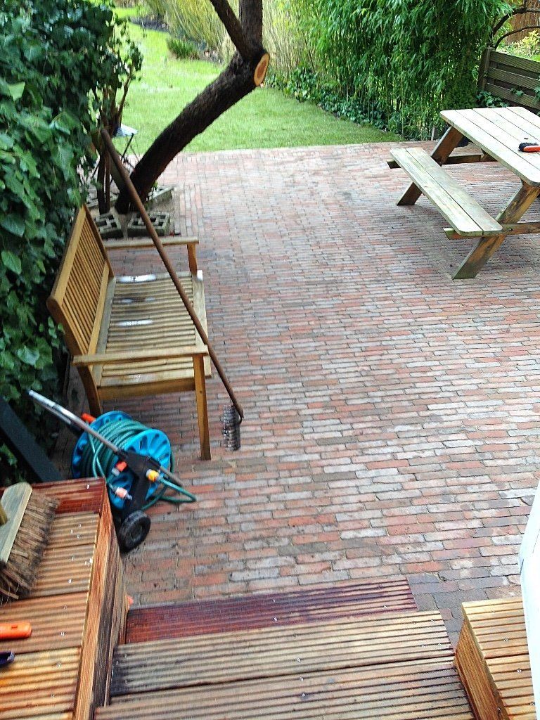 Een stenen terras met een houten bank, een picknicktafel en een trap ernaartoe, met een tuin en bomen.