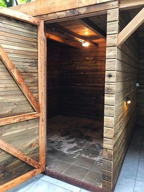 Houten buitenconstructie met openslaande deur, waardoor de tegelvloer en de plafondverlichting zichtbaar zijn.