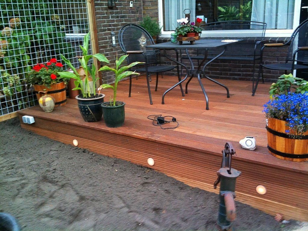 Houten terras met potplanten, tafel, stoelen en sfeerverlichting.