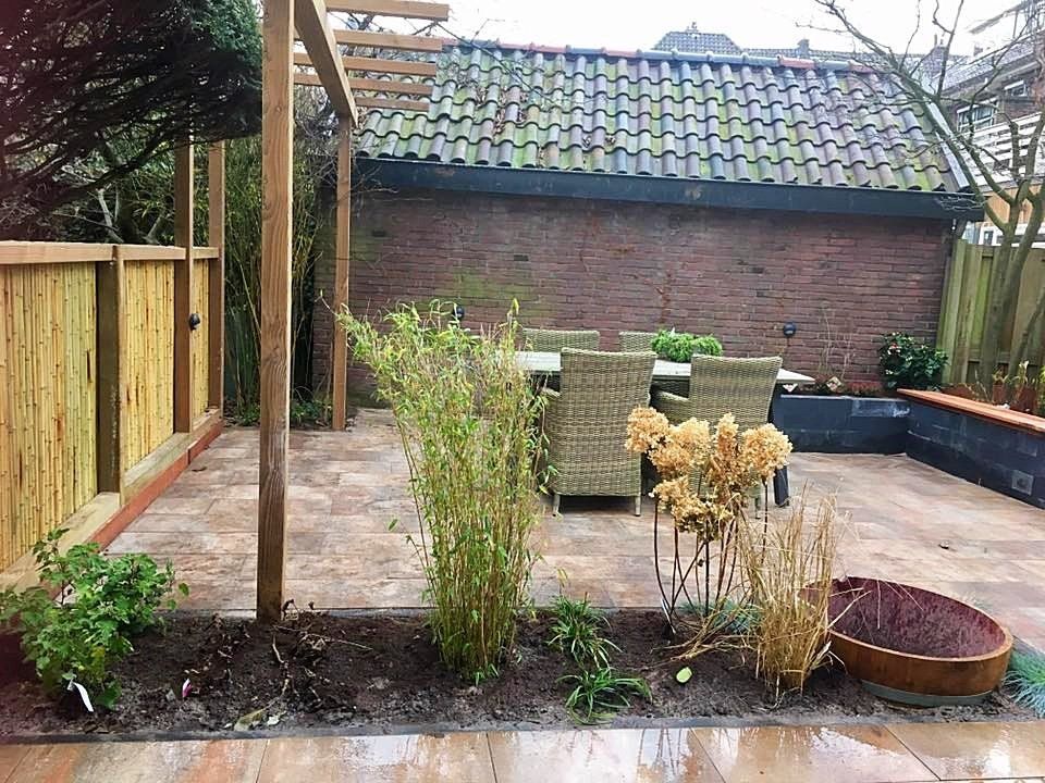 Terras in de achtertuin met houten schutting, eethoek en planten. Op de achtergrond een bruine bakstenen muur.