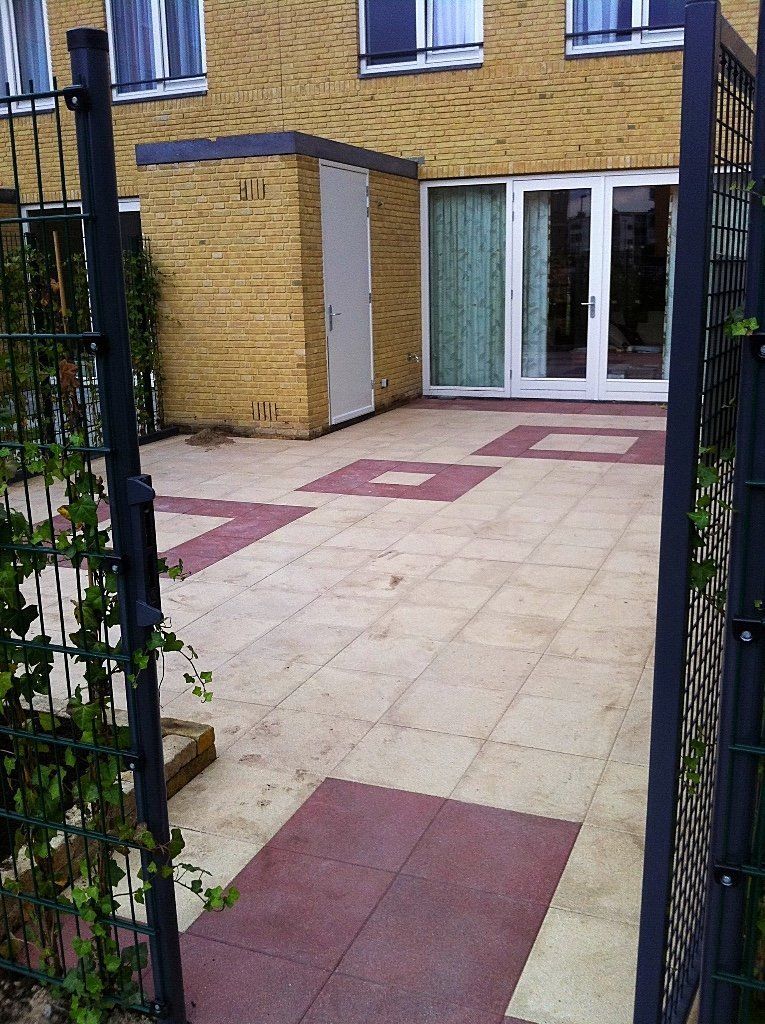 Terras met rode en beige tegels, een bakstenen gebouw en een zwart hek.