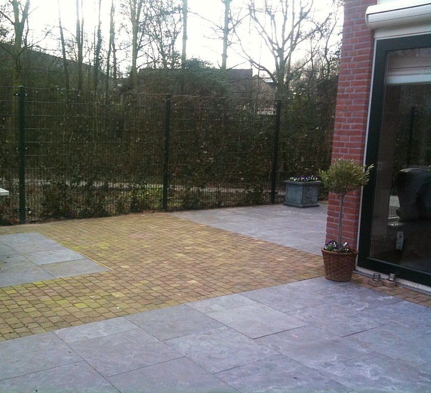 Terras met bestrating, bakstenen muur, potplant en uitzicht op een schutting en bomen.