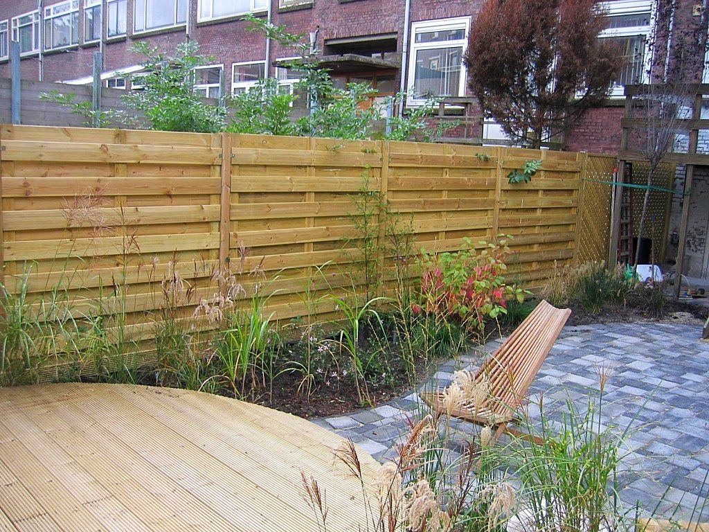 Houten schutting met planten in een kleine tuin; stoel en bestrating op de voorgrond.