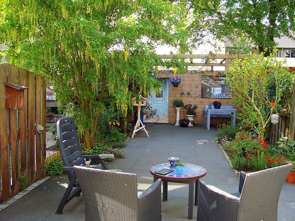 Gezellig terras met grijze stoelen rond een tafel. Een houten schutting en weelderig groen omringen het betegelde gedeelte.