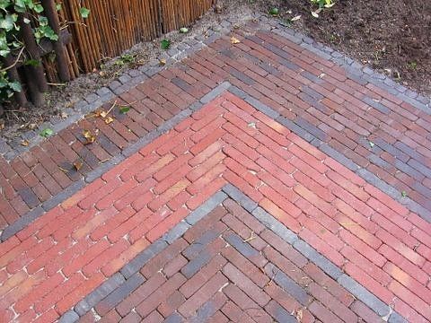 Bakstenen pad met visgraat- en randpatronen, uitgevoerd in rode en donkerbruine bakstenen.