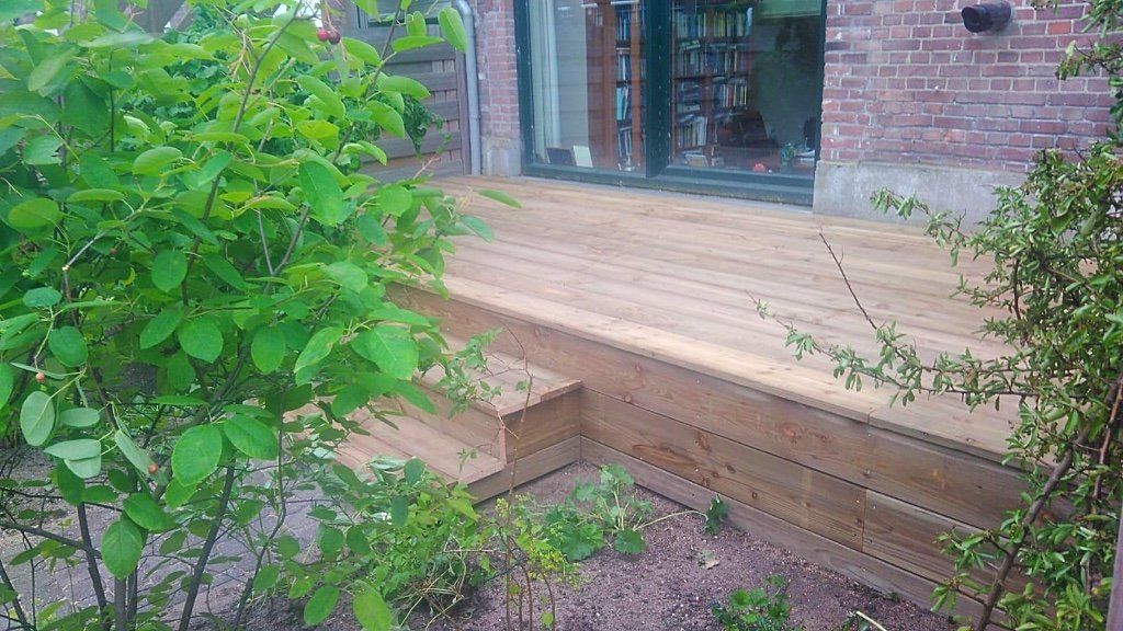 Houten terras met trap naast een huis met planten en groen.