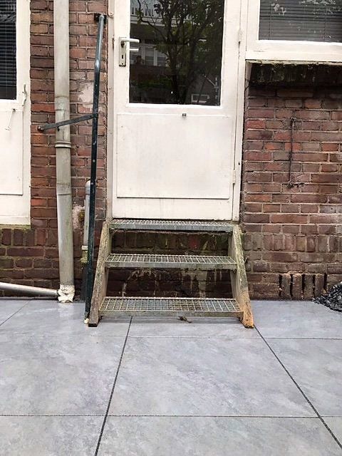 Metalen trappen die leiden naar een witte deur in een bakstenen gebouw.