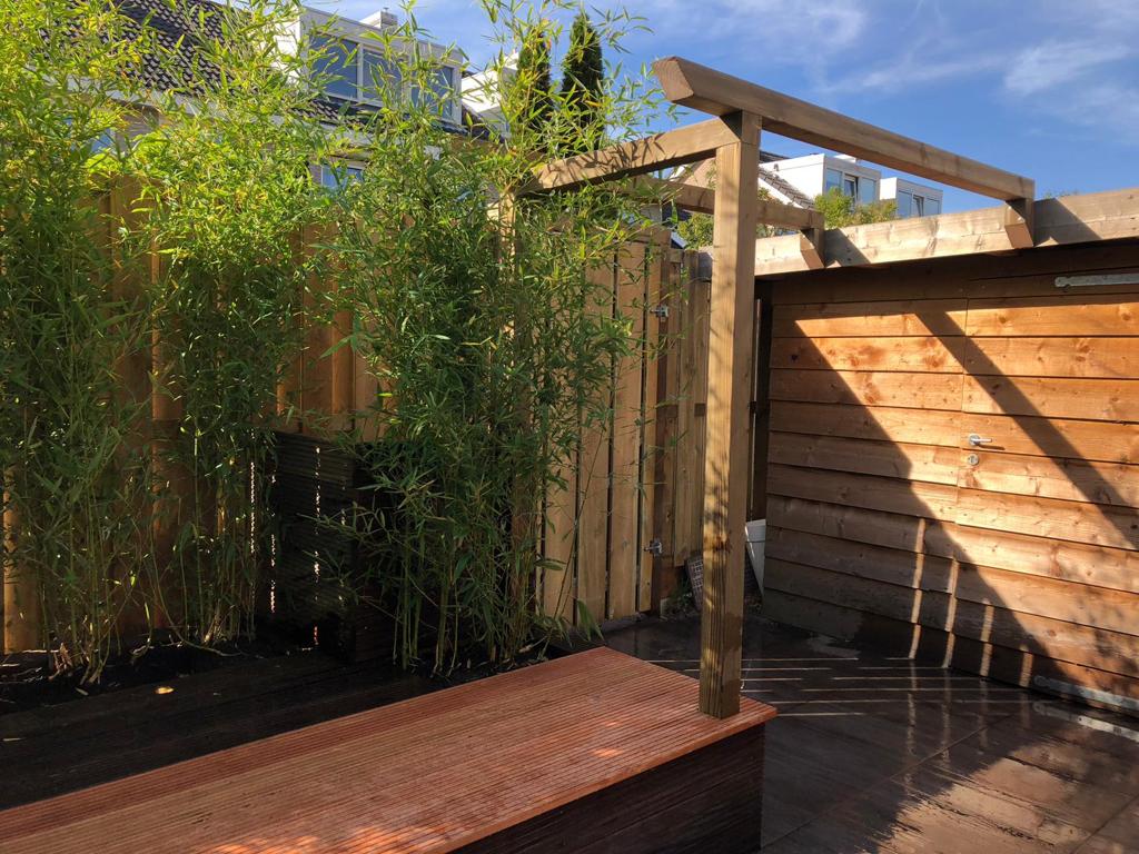 Houten schutting en pergola, bamboeplanten, zonnige buitenruimte.