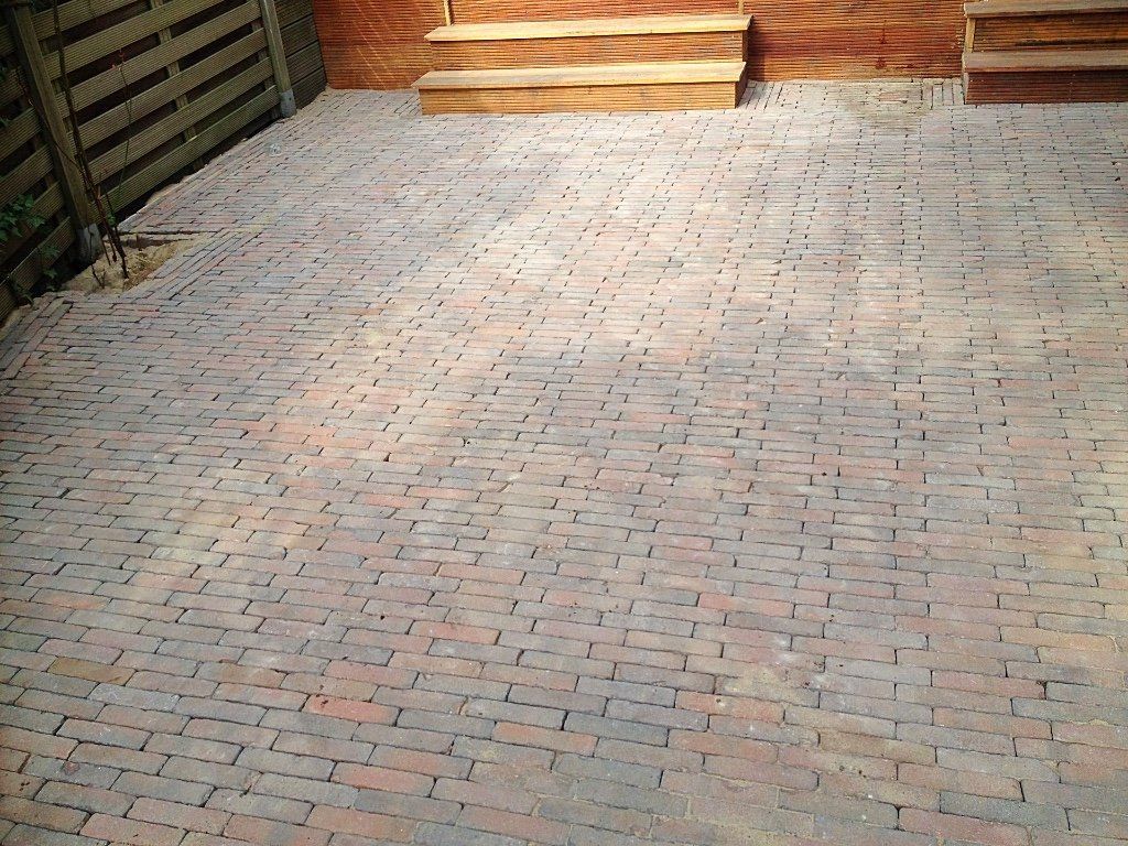 Binnenplaats met bakstenen bestrating en houten trappen, tegen een bakstenen en houten schutting.