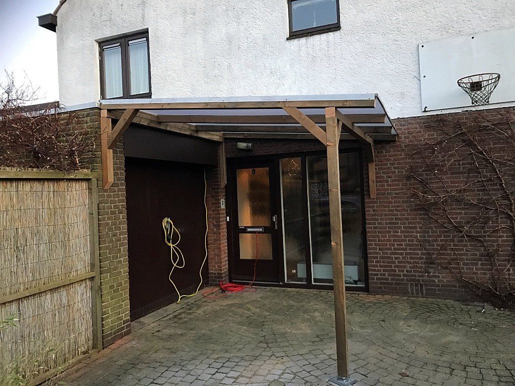 Houten carport boven een deur en garage; buitenkant van het gebouw van baksteen en stucwerk.