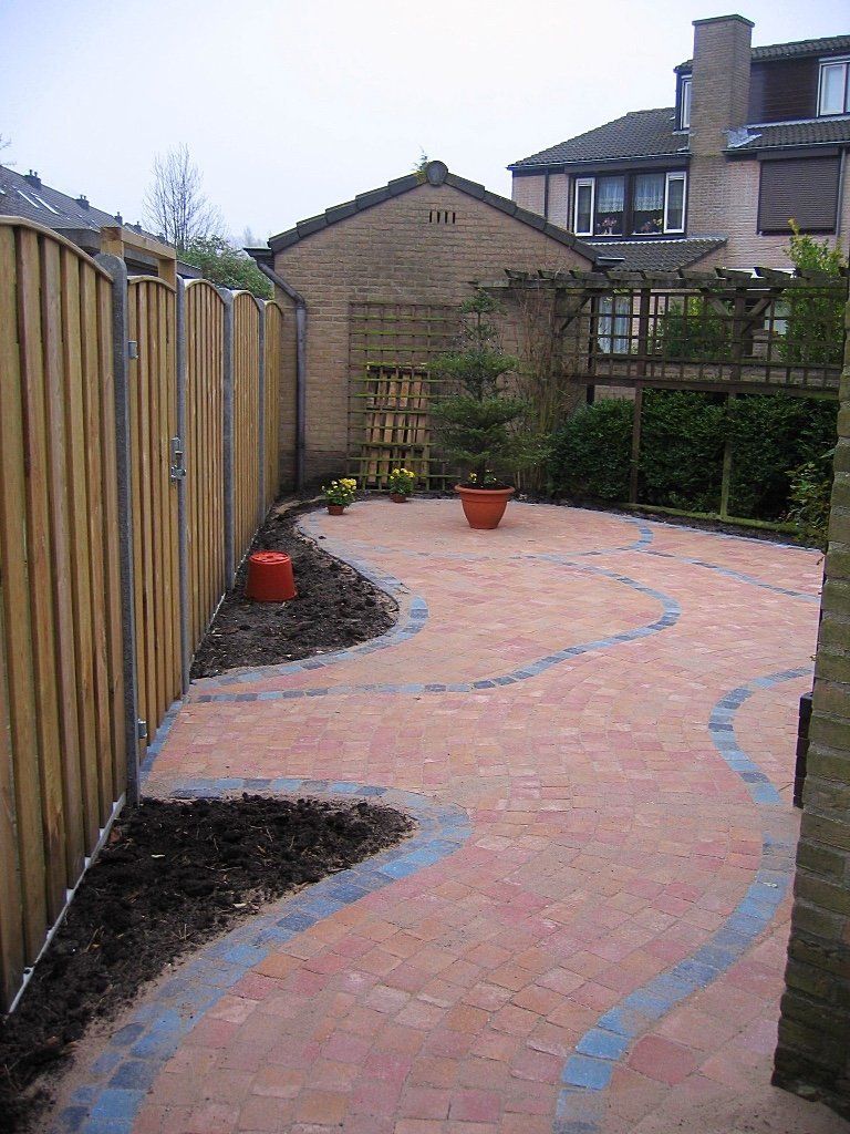 Een stenen terras met een kronkelend, blauw gemarkeerd pad, begrensd door een houten schutting en een kleine tuin met een terracotta pot.