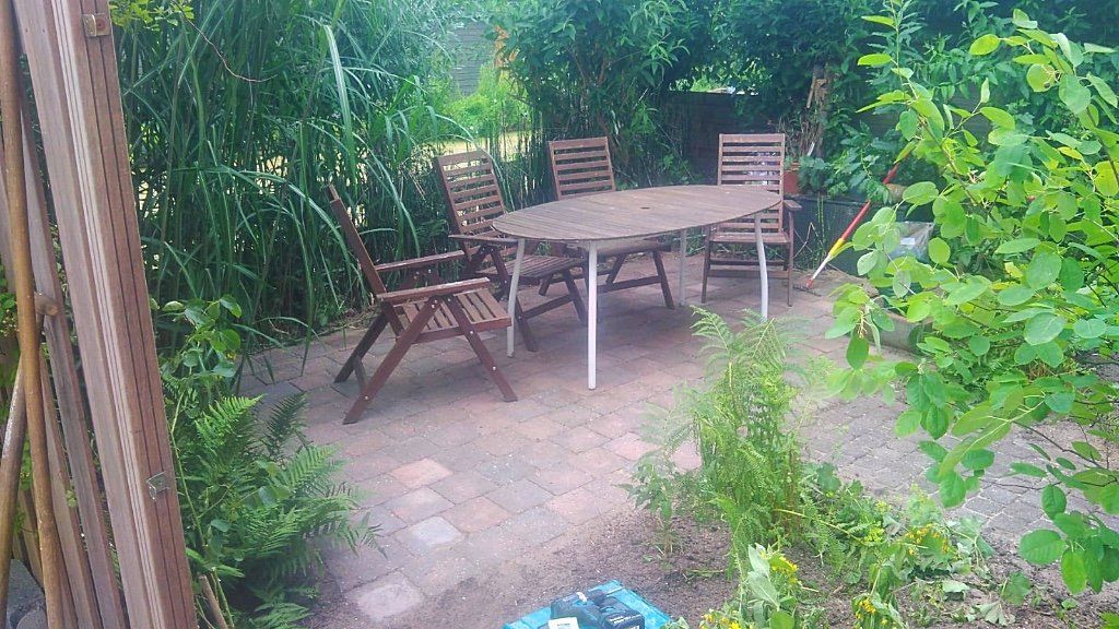 Terras met houten tafel en stoelen, omgeven door weelderig groen.