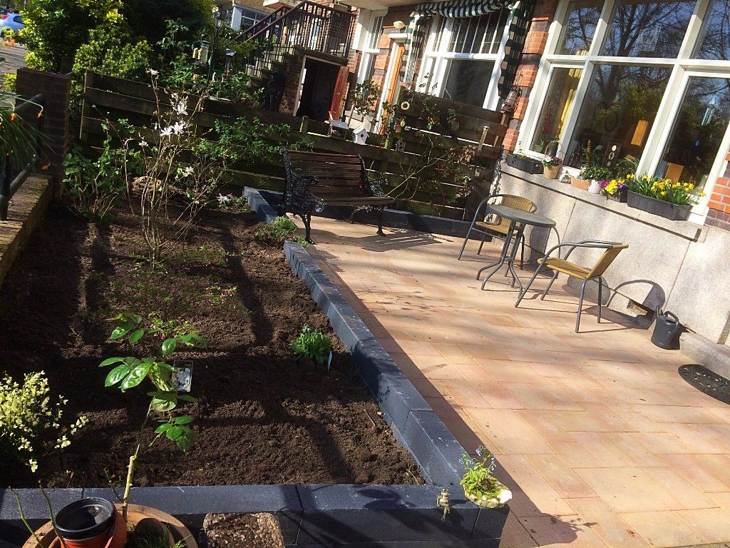 Een bloembed met jonge plantjes naast een terras met zitjes. Zonnige dag.