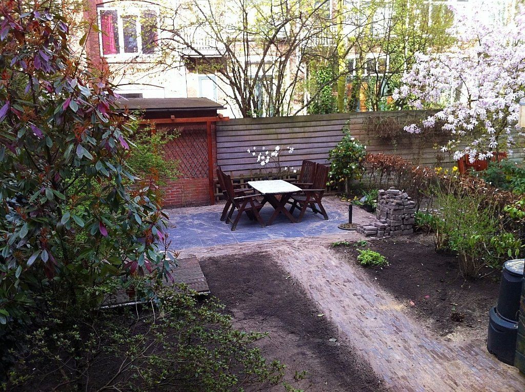 Terras met donkerhouten tafel en stoelen, begrensd door een bakstenen pad en een weelderige tuin.