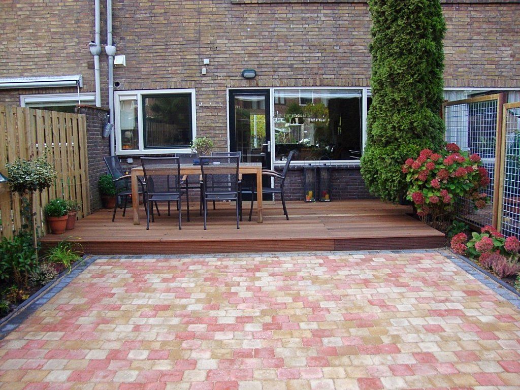 Terras in de achtertuin met houten vlonder, tafel, stoelen en een stenen pad.