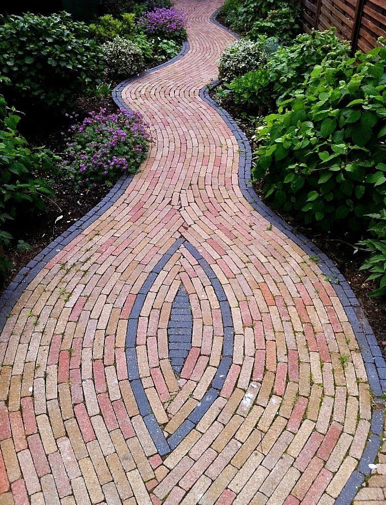 Een bakstenen pad met een centraal ovaal ontwerp, bekleed met donkere bakstenen, slingert door een tuin.