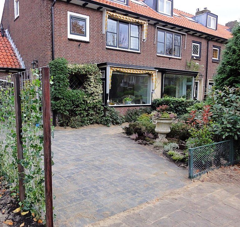 Bakstenen huis met bestrate oprit en tuin. Een muur is begroeid met groen.