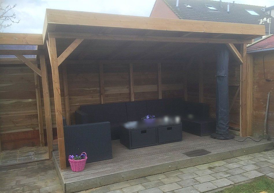 Houten buitenverblijf met zwart meubilair, waaronder een bank en een tafel, op een stenen terras.