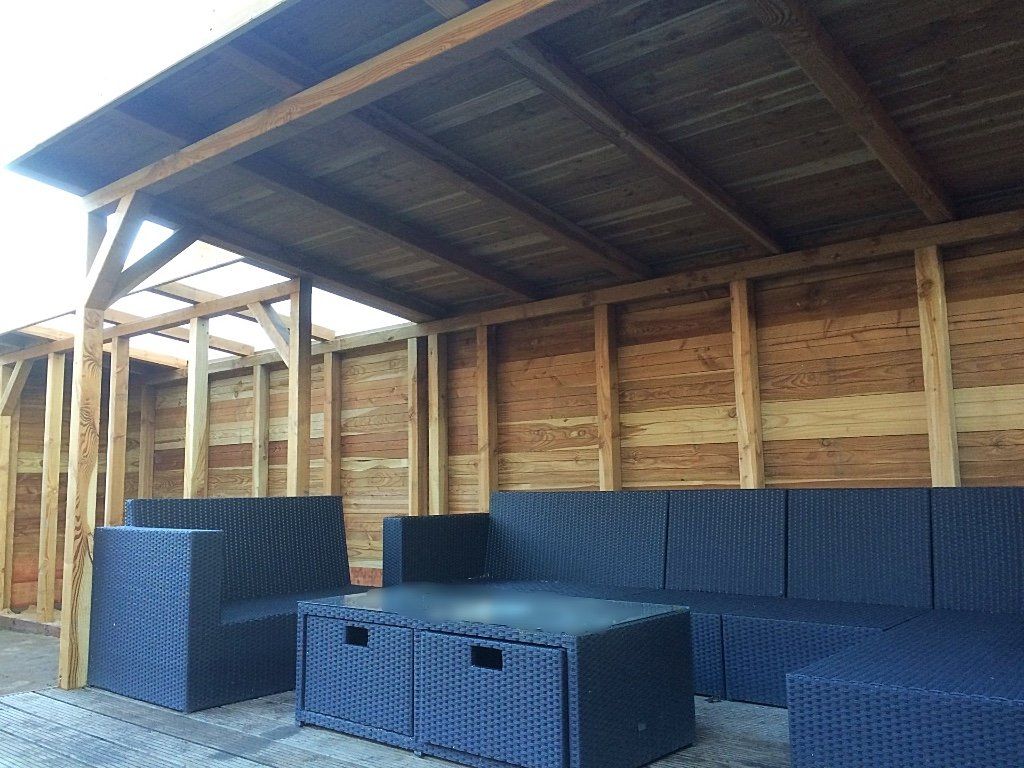 Een zitgedeelte buiten met zwart rieten meubilair onder een houten dak.