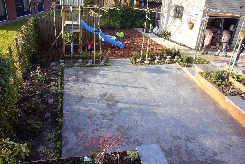 Achtertuin met speeltuin, terras en bloembedden. Mensen in de buurt van de garage.
