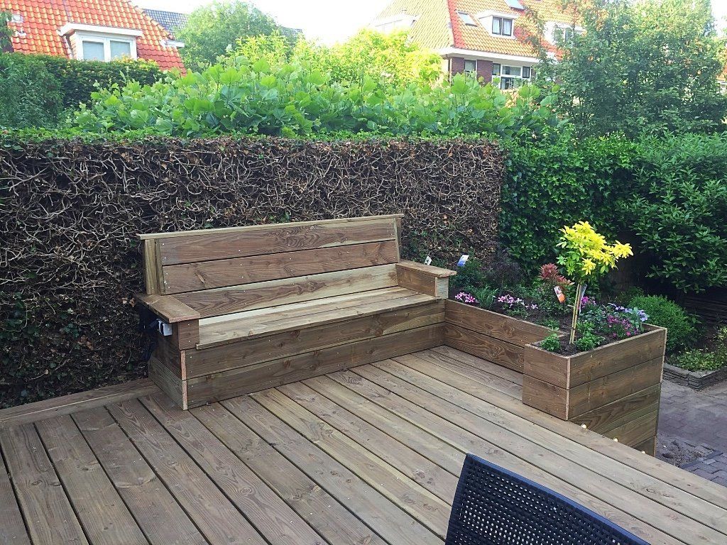 Houten bank en plantenbak op een terras, met een heg en een huis op de achtergrond.