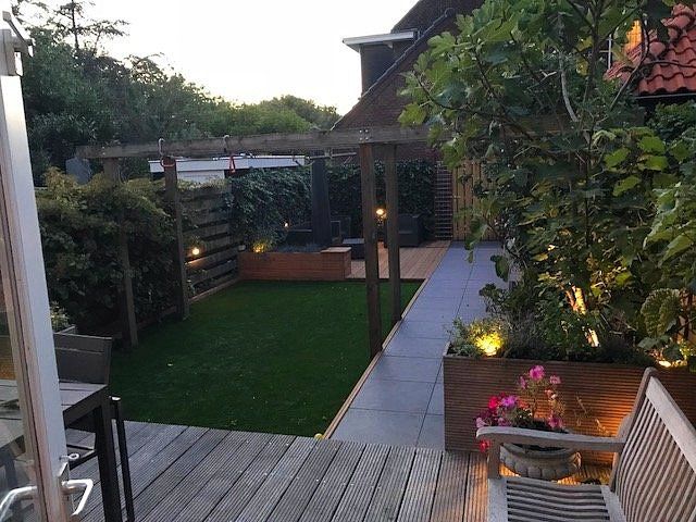 Een achtertuin met een houten terras, een pergola en een stukje groen gazon.