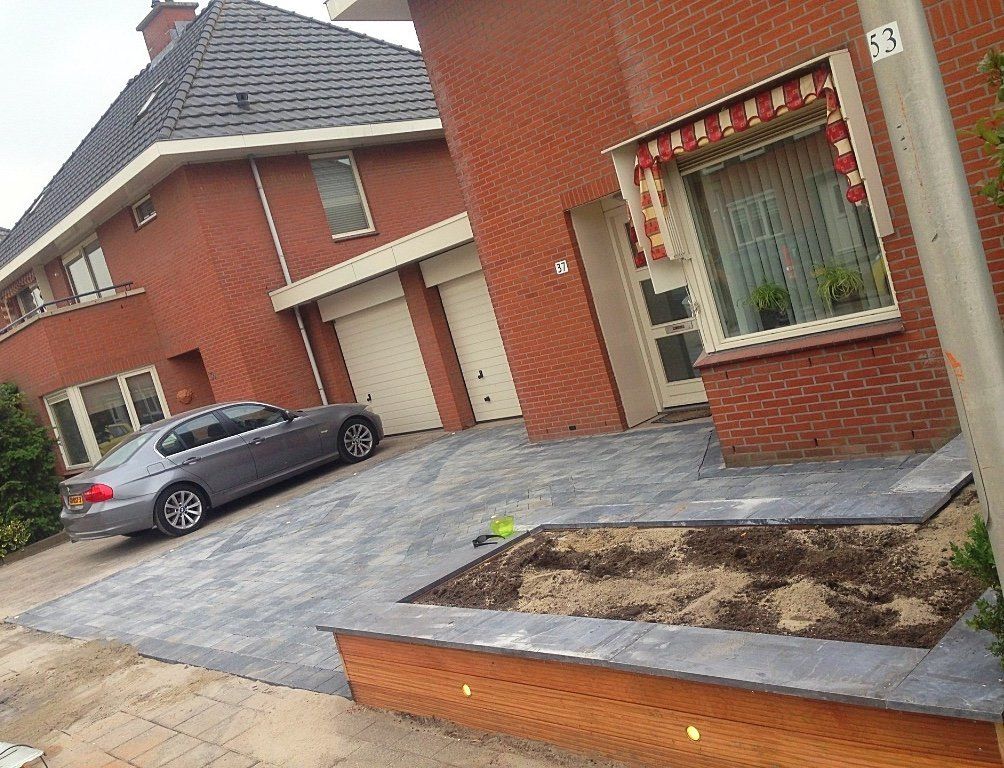 Een grijze auto geparkeerd op de oprit voor een bakstenen huis met een bloembed.